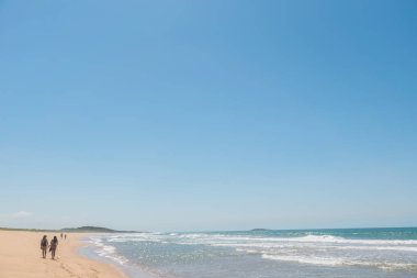 Mavi gökyüzü, iki kadın yürümek, bunlardan biri bir sırt çantası taşır ve bir şapka giyer, çok ileride başka bir çift de yürüyüş ve Paulo Cezar Vinha parkta ayak izleri bırakarak, Setiba, Espirito Santo