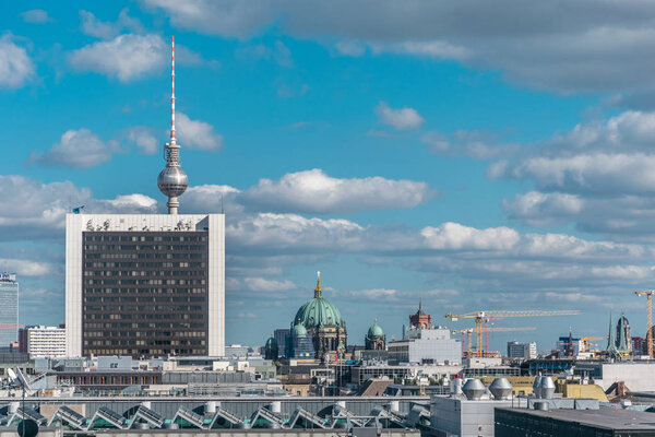Urban landscape of the busy city of Berlin, with a lot of metal elements like the famous Berlin TV Tower and its iconic sphere, construction tower cranes and the Berliner Cathedral in the background.