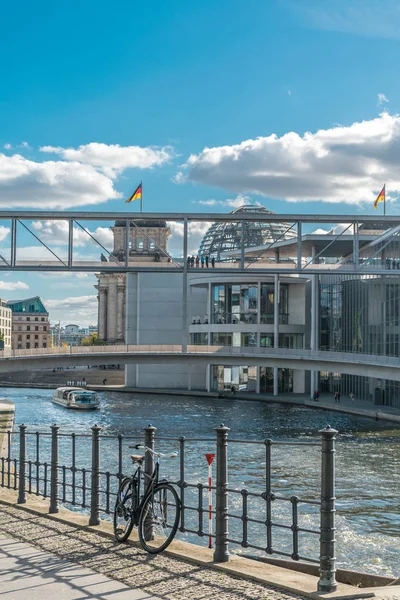 Veduta panoramica di una bicicletta appoggiata a una recinzione metallica, con una barca nel fiume Sprea e l'architettura metallica del parlamento tedesco con bandiere nazionali sul tetto sullo sfondo — Foto Stock