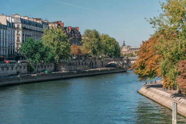 Perspectiva do rio Sena natural entre o ambiente urbano de Paris, França, com árvores voluptuosas e pessoas relaxando nas margens perto de edifícios clássicos durante o dia — Fotografia de Stock