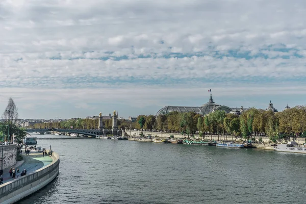 Panoramica distinta dei riflessi della luce solare sulla Senna, vicino al ponte Alessandro III e al Grand Palais con molte barche, numerosi alberi allineati e nuvole in un cielo blu — Foto Stock