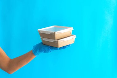 Konteynırlarda kurye teslimatı. Mavi arka planda konteynırları tutan kurye kız. Kendi kendini izole eden bir teslimat. Bir gönüllü yemek getiriyor. Yemek teslimatı konsepti. Paket yemek..