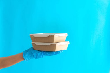 Konteynırlarda kurye teslimatı. Mavi arka planda konteynırları tutan kurye kız. Kendi kendini izole eden bir teslimat. Bir gönüllü yemek getiriyor. Yemek teslimatı konsepti. Paket yemek..