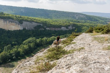 Genç bir adam uçurumun kenarında oturuyor. Dağcılık ve turizm kavramı. Güzel dağ manzarası. Olağanüstü bir spor. Metanet. Yalnız seyahat etmek..