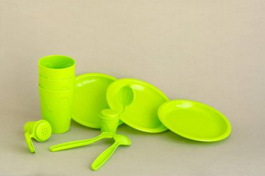 Gri nötr bir arkaplanda yeşil plastik sofra takımı. Yeniden kullanılabilir plastik piknik tabakları. Çevre kirliliği. Paket yemek. Açık hava eğlencesi için sofra takımı.