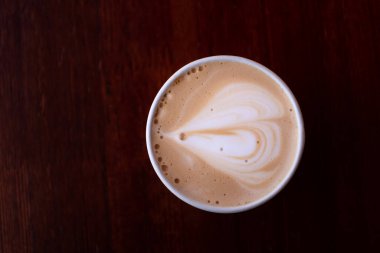 Tek kullanımlık kapuçino, tek kullanımlık kupa manzaralı. Kahvenin köpüğündeki kalp. Metin için boşluk olan üst görünüm. İyi ruh hali kavramı. Mağazanın tezgahından bir fotoğraf..