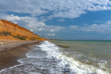 Deniz kıyısında dalgalar ve kumlar. Fırtınalı denizi olan güzel bir yaz manzarası. Parlak güneş ve mavi gökyüzü. Çamur yüksek kıyıları. Kırım Plajları