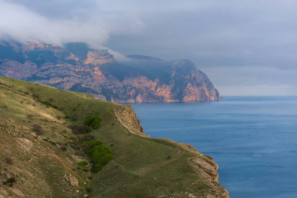 Cape ay-ya Kırım Balaklava. Deniz kıyısı ve bulutlu dağlar. Gün batımında manzara çok güzel. Dağda alçak bulutlar. Deniz kenarındaki patika.
