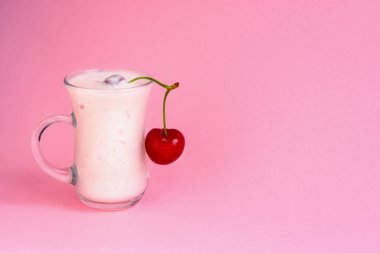 Pembe arka planda vişneli yoğurt. Kirazlı lezzetli bir süt içeceği. İzole edilmiş parlak pembe bir arka plan. Sağlıklı beslenme. Yaz serinletici içecek.