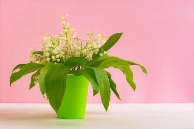 Pembe arka planda bir bardak içinde vadideki zambaklar. Bahar çiçeklerinin ön düzenlemesi. Güzel ve parlak doğal bir arka plan. Taze çiçekler.