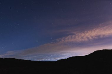 Yıldızlı gecede Neowise Kuyruklu Yıldızı. Gün batımından sonra dağda yeşil kuyruklu yıldız ve pembe bulutlarla yatay çerçeve. Şehrin üzerinde alacakaranlık.