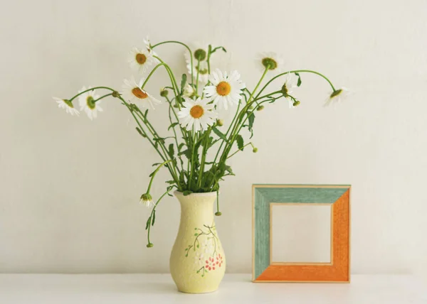 A bouquet of daisies in a vase on the table. Rural vintage still life. Horizontal composition for the design of the cards. White table and white concrete background with space for text.