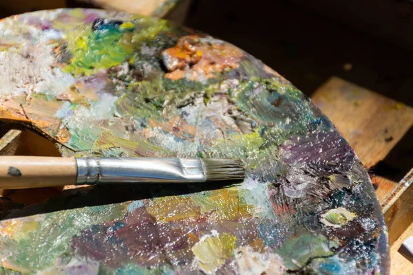 Brushes on the artist\'s palette. Plein air sketchbook with paints. Mixing oil paints. Creative process of drawing in nature. Autumn plein air.