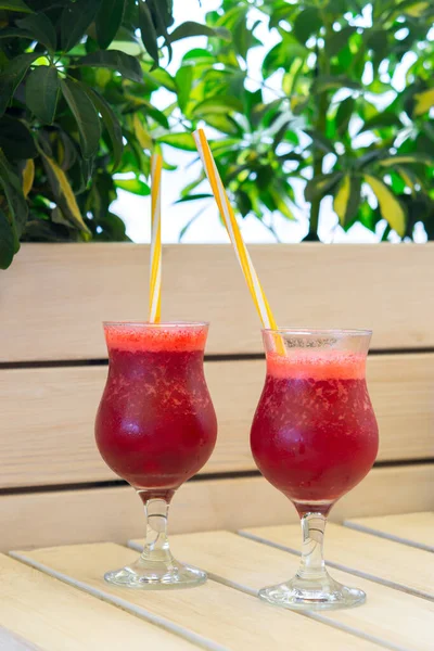 Berry smoothies in glass glasses. Summer refreshing drink. Two glasses with tubes on the blurred background of a summer cafe. Vitamin vegetarian cocktail.