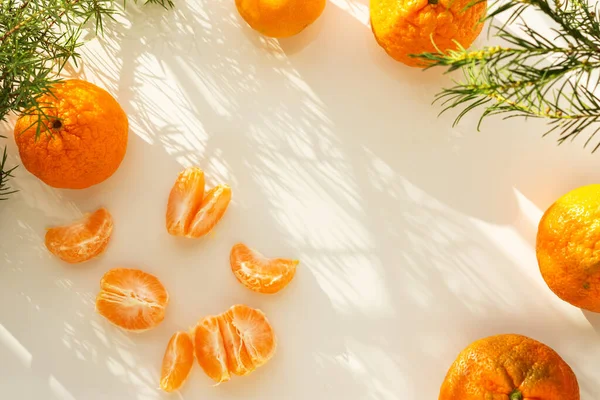 Mandalina ve Noel ağaçlarının Noel kompozisyonu. Parlak tatil kartı. Mandalinaların ve Noel ağacı dallarının en üst görüntüsü. Yeni yılın tasarımı. Güneşin güzel gölgeleri beyaz bir masada.