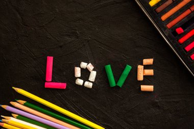 Siyah arka planda çok renkli pastel boya kalemleri. Aşk kelimesi pastel boyalardan yapılır. Aşkın ve birliğin sembolü. Genişletilmiş yatay afiş. Sevgililer Günü tebrik kartının yaratıcı düzeni.