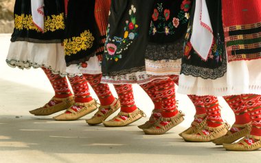Bulgar folkloru. Dans eden kızlar. Geleneksel kostümlü insanlar Bulgar halk dansları yapıyor. Bulgar halk dansları için geleneksel ayakkabı, çorap ve kostümlü kadın bacaklarının yakın çekimi.
