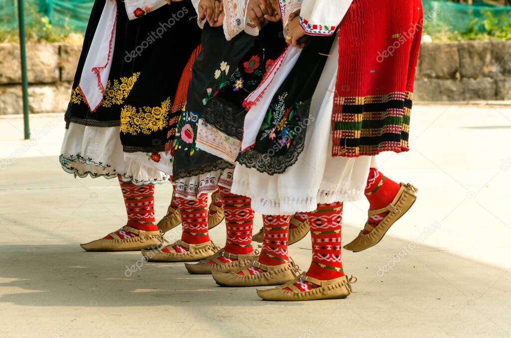 Bulgarian folklore. Girls dancing folk dance. People in traditional costumes dance Bulgarian folk dances. Close-up of female legs with traditional shoes, socks and costumes for Bulgarian folk dances.