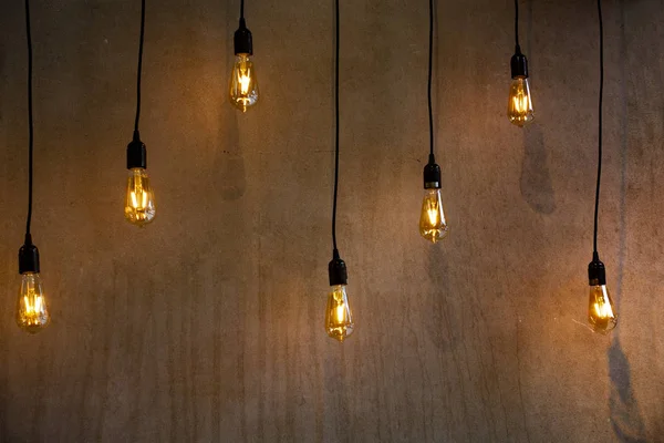 hanging lighted bulbs near a cement wall hanging from their black power wire