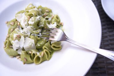 Rigatoni makarna çanak çatal çam fıstığı peynir beyaz plaka pesto kefalet sos