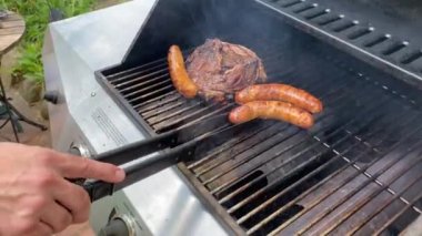 Yaşam tarzı yaz adamı propan gazı ızgarasında kazık ve sosis pişiriyor metal dilleri deliğe sokuyor.