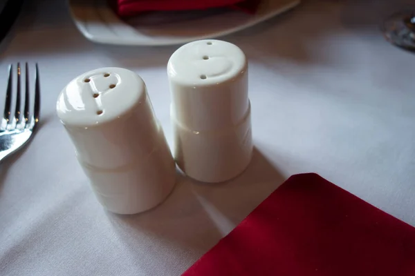  Seramik beyaz baharat karıştırıcılar kırmızı peçeteli beyaz bez masanın üzerinde oturuyorlar.