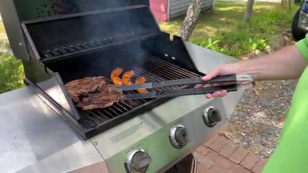 ライフスタイル夏屋外男調理ステークスとソーセージプロパンガスグリル金属舌を保持 — ストック動画