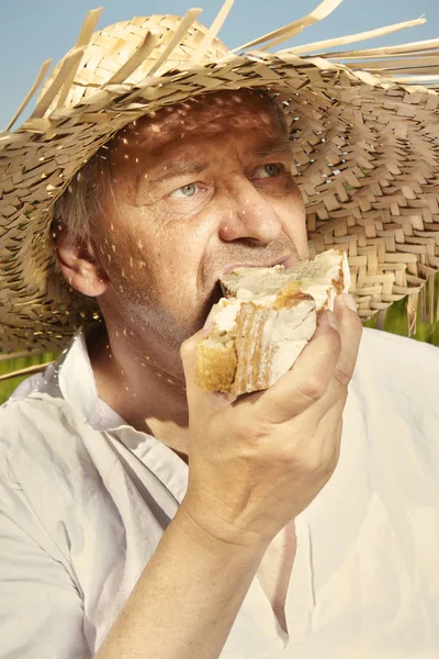 Village natural country man on summer meadow eating bread after mowing grass
