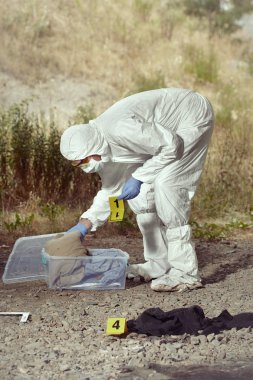 Criminologist technician in DNA free protective suit collecting evidences of probable criminal act clipart