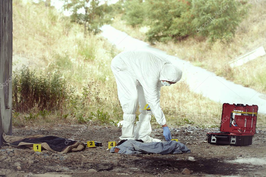 Criminologist technician in DNA free protective suit collecting evidences of probable criminal act