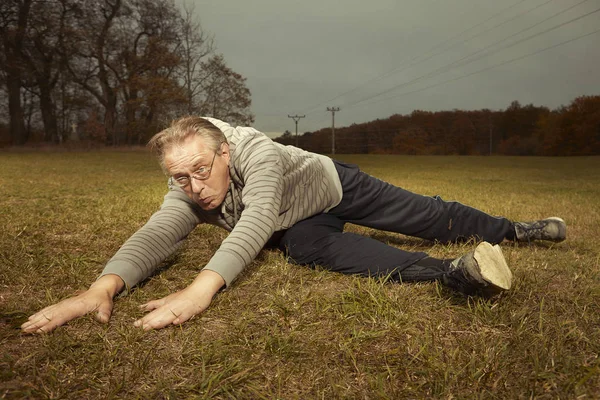 Aging older man exercising in sportsuit outdoor on meadow