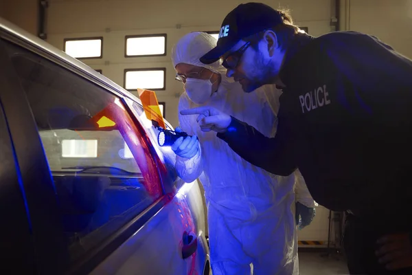 刑事调查 警察技术员在带有 灯的车库的可疑汽车上向同事留下指纹 — 图库照片