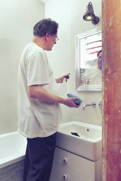 Older poor man cleaning his home with cleaner and sponge