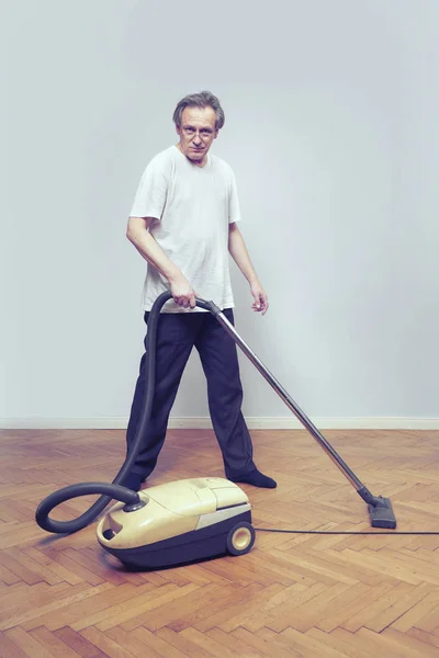 Older poor man cleaning his home with vacuum cleaner