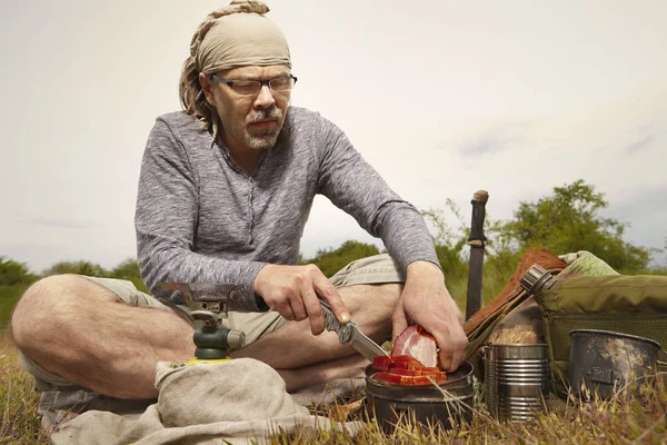 Mature man on trip in summer wilderness preparing food
