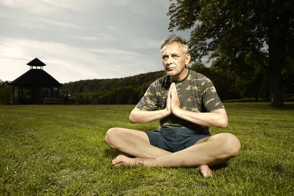 Older man practicing meditation rituals in summer city park