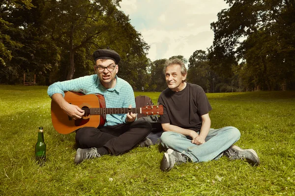 两名男子在城市公园的夏季草地上 用吉他享受这一天 — 图库照片