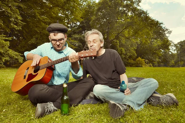市公園の夏の牧草地で2人の男性がギターで一日を楽しむ — ストック写真