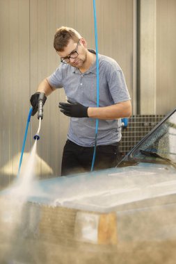 Oto yıkamadaki adam eski güzel arabasıyla ilgilenir.