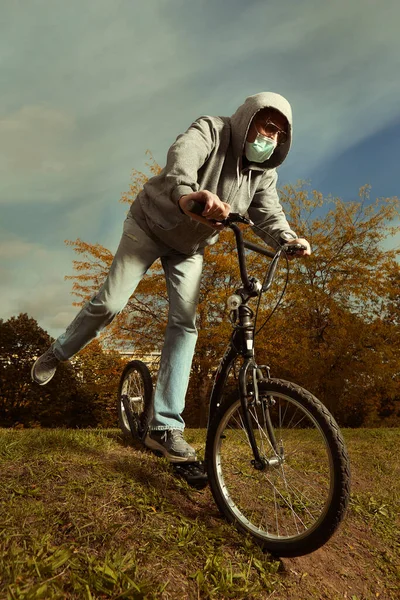 Older city man vagabond in hooded shirt with mask on scooter