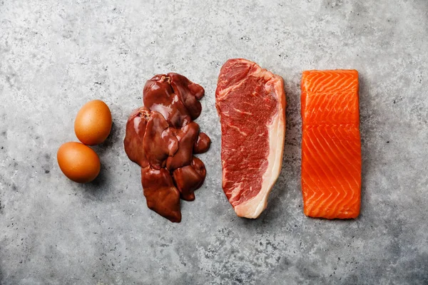 Raw food selection for Ketogenic diet Egg, Chicken Liver, Beef meat Steak and Salmon fish Steak on gray concrete background — Stock Image Raw Food Selection Ketogenic Diet Egg Chicken Liver Beef Meat Stock Picture
