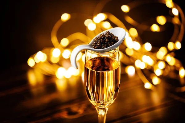 Black caviar in porcelain spoon and glass of champagne Buffet table style on Holiday Christmas sparkling lights background bokeh