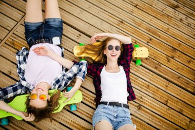 İki şık genç kentsel kızla longboards sokakta ahşap döşeme yalan. Arkadaşları eğlenmek ve yaz tatillerinde birlikte zaman geçirin