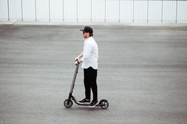 Homem moderno em roupa elegante preto e branco montando scooter elétrico na cidade — Fotografia de Stock