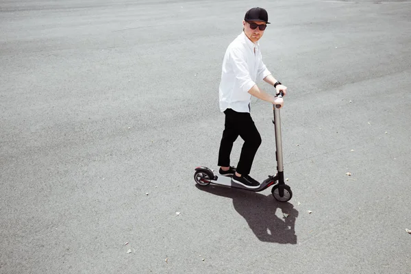 Homem moderno em roupa elegante preto e branco montando scooter elétrico na cidade — Fotografia de Stock