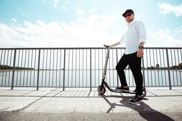 Сучасний чоловік одягнений у білу сорочку і чорні штани, що стоять на вулиці з електричним скутером — стокове фото