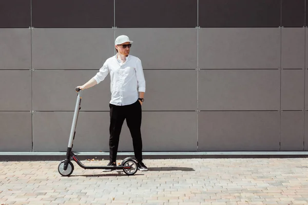 Pria modern mengenakan kemeja putih dan celana hitam berdiri di jalan dengan skuter listrik — Stok Foto