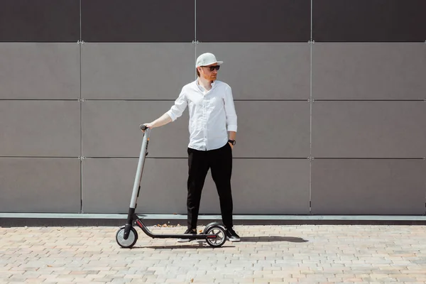 Hombre moderno vestido camisa blanca y pantalones negros de pie en la calle con scooter eléctrico —  Fotos de Stock