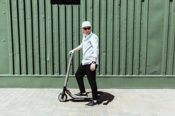 Homem moderno vestido camisa branca e calças pretas de pé na rua com scooter elétrico — Fotografia de Stock