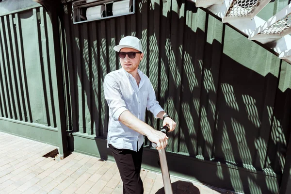 Moderní muž na sobě bílou košili a černé kalhoty, stojící na ulici s elektrický skútr — Stock fotografie